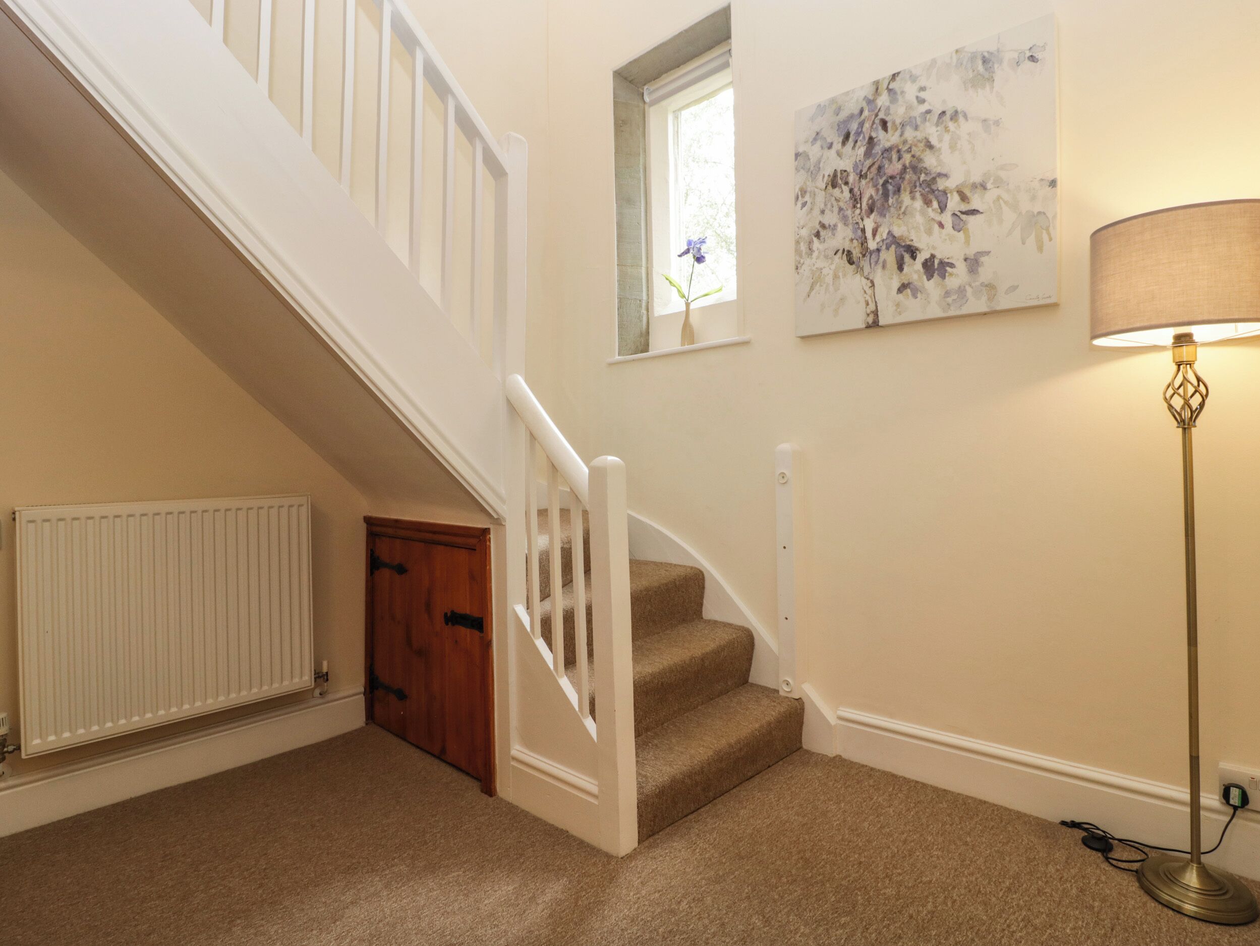 A staircase with white railings, carpeted steps, a radiator, a wooden door, a painting, and a floor lamp.