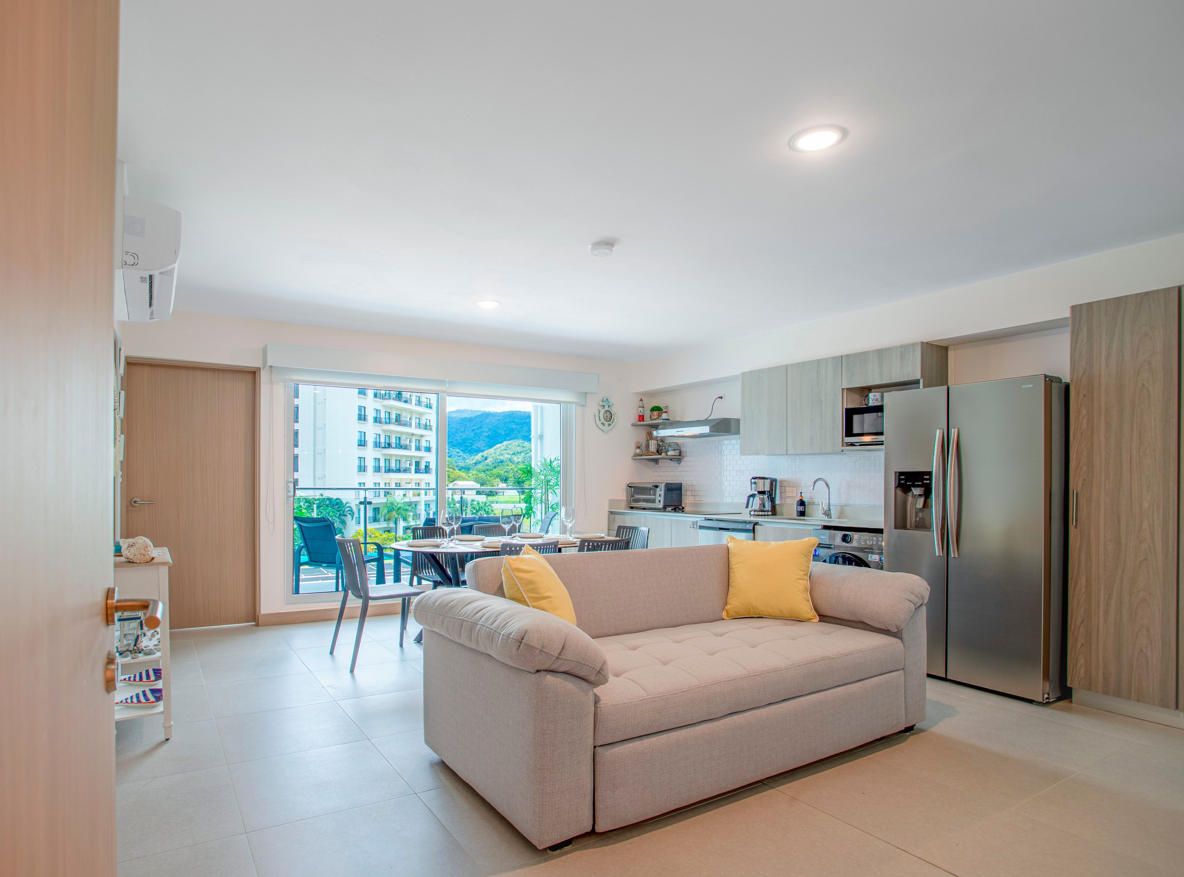 A modern apartment with a kitchenette, a dining area, and a sofa with yellow cushions.