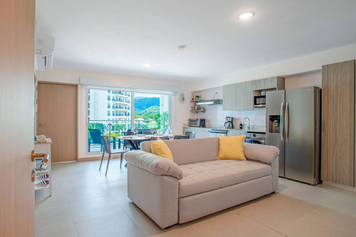 Een modern appartement met een kitchenette, een eethoek en een bank met gele kussens.