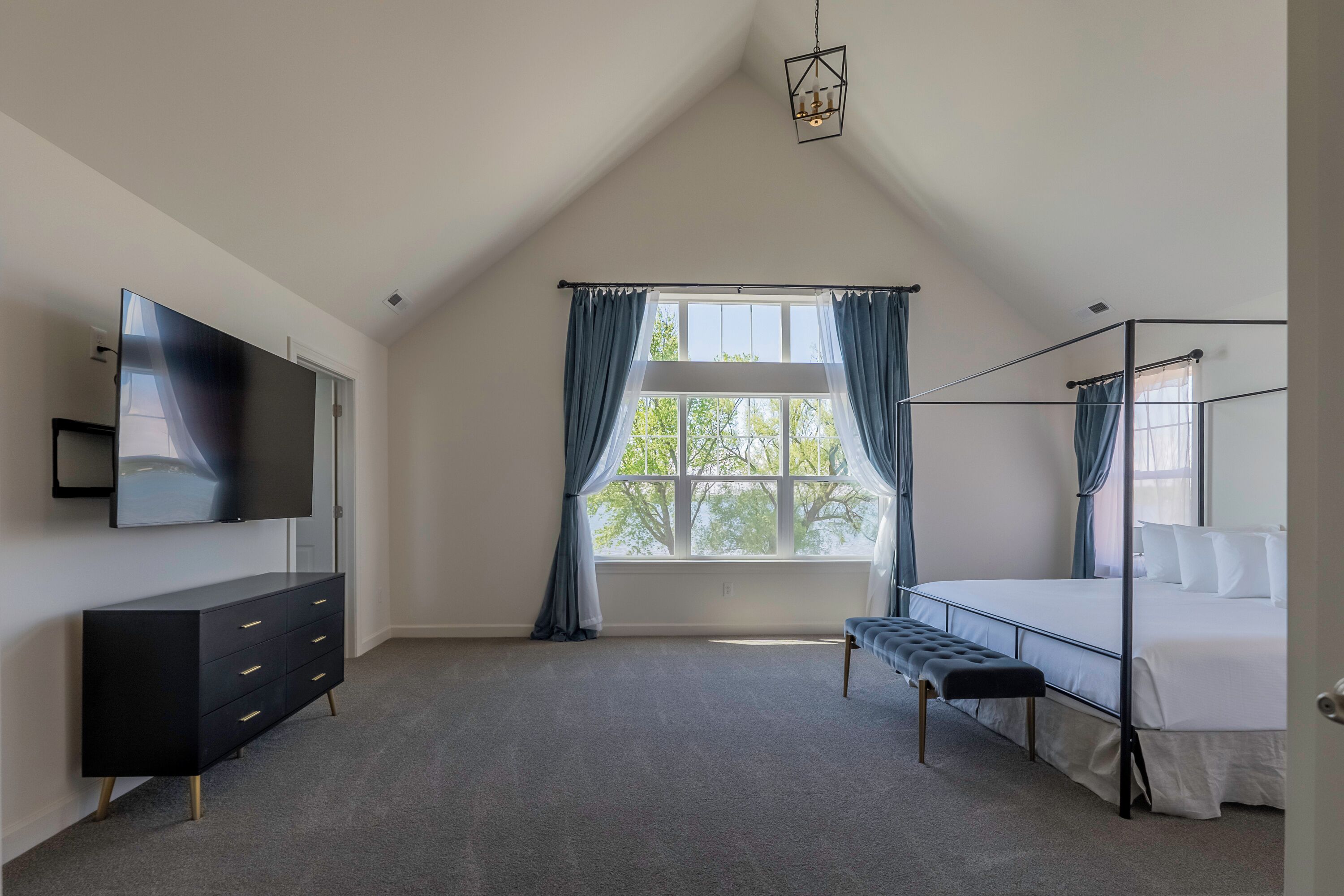 Une chambre à coucher avec un lit, une télévision, une commode et une fenêtre avec des rideaux.