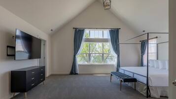 Une chambre à coucher avec un lit, une télévision, une commode et une fenêtre avec des rideaux.