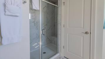 Un baño con cabina de ducha de vidrio, una puerta blanca y un perchero con toallas dobladas.