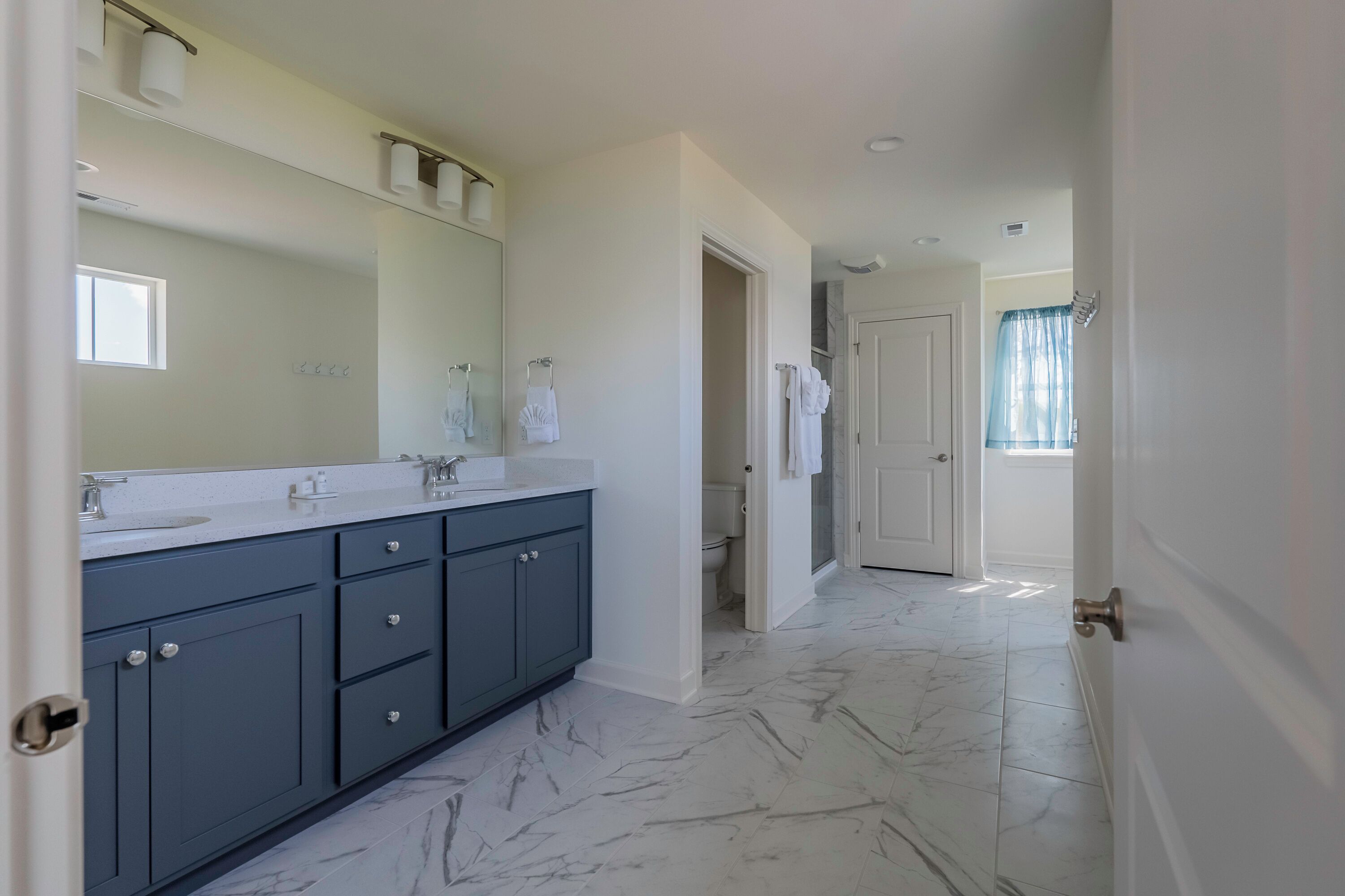A modern bathroom with a large mirror, dark blue cabinets, and a marble floor.