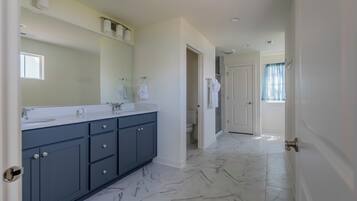 A modern bathroom with a large mirror, dark blue cabinets, and a marble floor.