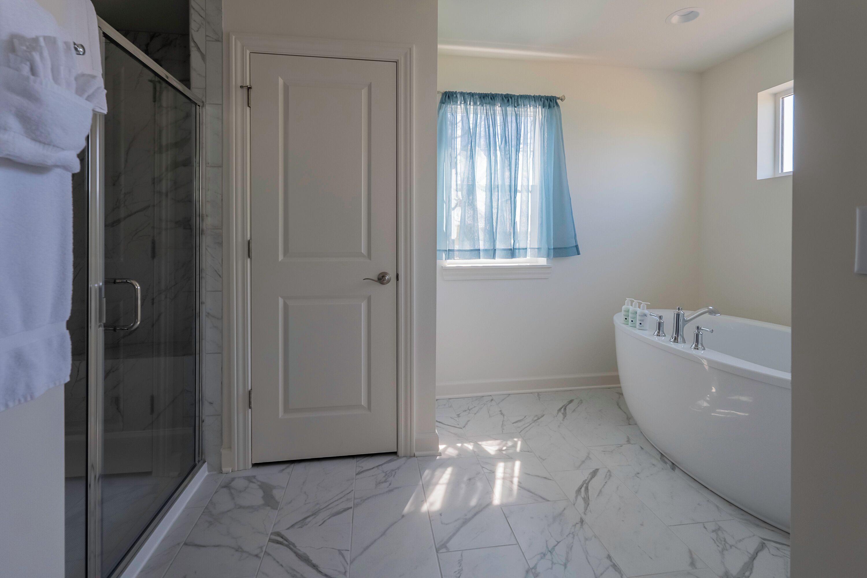 A bathroom with a shower, a bathtub, and a window with curtains.