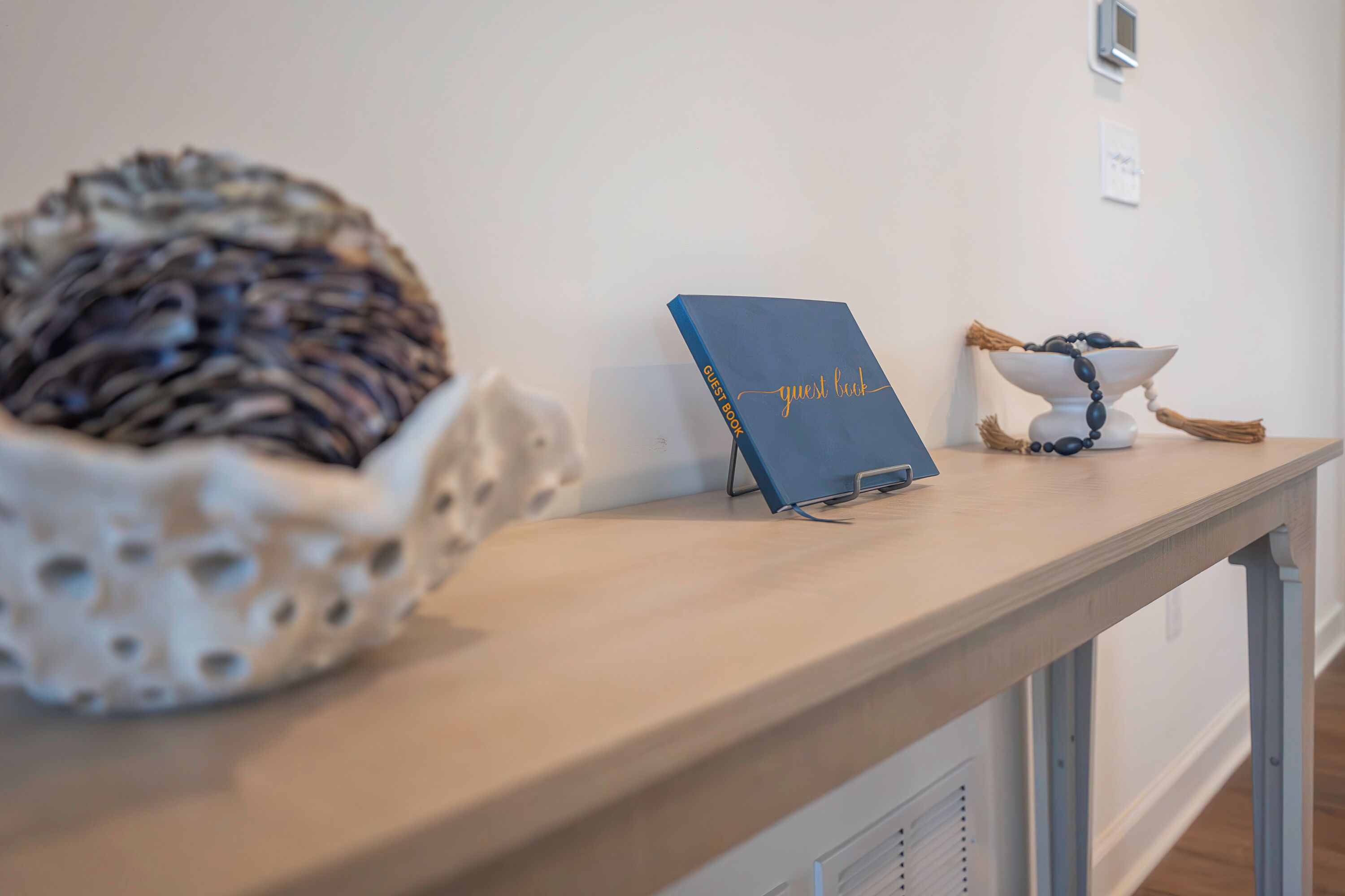 A wooden table with a blue guest book, a decorative bowl, and a white ceramic piece.