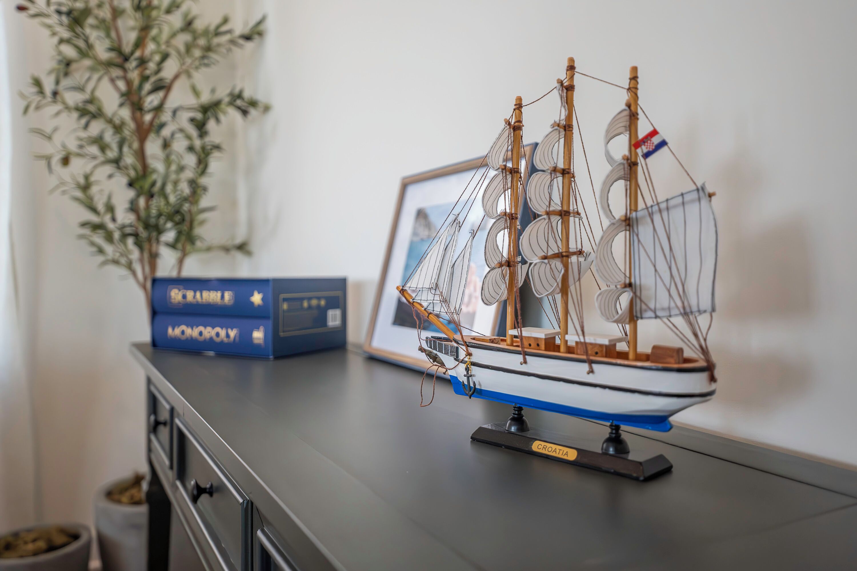 A model ship on a table with Monopoly boxes and a framed picture in the background.