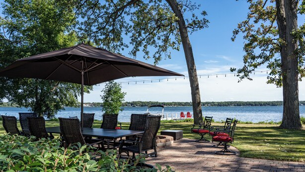 A patio with a table and chairs, a large umbrella, and a view of a lake.