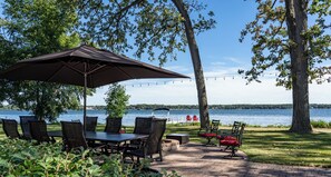 A patio with a table and chairs, a large umbrella, and a view of a lake. - Lake House (Delavan)