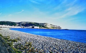 A coastal scene with a pebble beach, a large building with a white facade, and cliffs in the background.