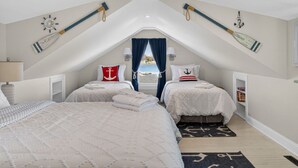 A bedroom with two beds, nautical decor, a view of the sea, and a sloped ceiling.