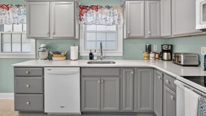 A kitchen with grey cabinets, a dishwasher, a sink, and a toaster.