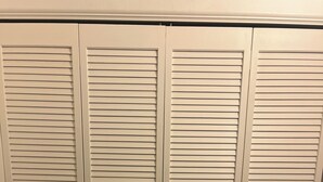 Un ensemble de quatre portes de placard blanches à persiennes, dotées d’une poignée centrale.