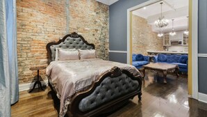 Un dormitorio con pared de ladrillo, una cama con cabecera oscura, un sofá azul y una mesa de centro de madera.