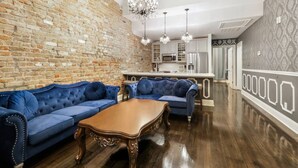 Un salón espacioso con pared de ladrillo, un conjunto de sofá azul, una mesa de centro de madera y una araña.