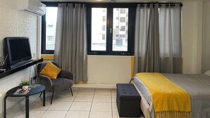 Une chambre d’hôtel moderne équipée d’un lit, d’un bureau avec un ordinateur, d’une chaise et d’un ventilateur de plafond.