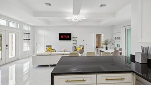 A modern kitchen with a black countertop, white cabinetry, and gold handles. There is a large island with a black top and gold handles.