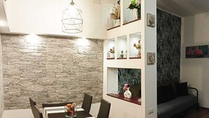 A dining area with a stone wall, a dining table with chairs, a hanging light fixture, and a sofa in the background. - Apartment a stone's throw from S.Giovanni (Roma)