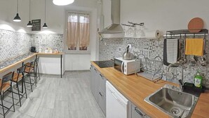 A modern kitchen with a wooden countertop, a built-in oven, and a sink. There are bar stools and a window with curtains. - Apartment a stone's throw from S.Giovanni (Roma)