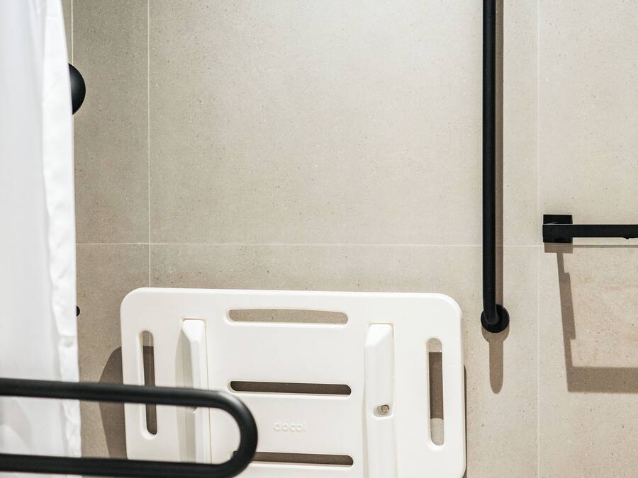 Een badkamer met een wit toilet, een witte handgreep en een zwarte leuning.