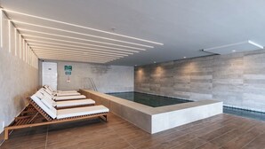 Ein moderner, überdachter Schwimmbereich mit mehreren Liegestühlen und einer Holzterrasse.