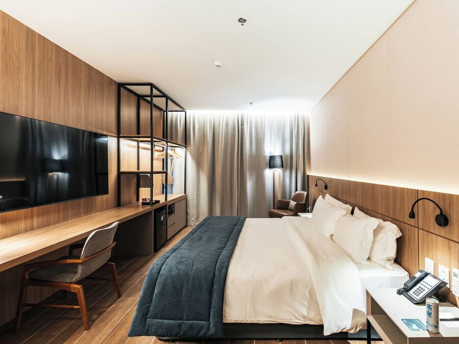 A modern hotel room with a large bed, a desk with a chair, a flat-screen TV, and a bedside telephone.