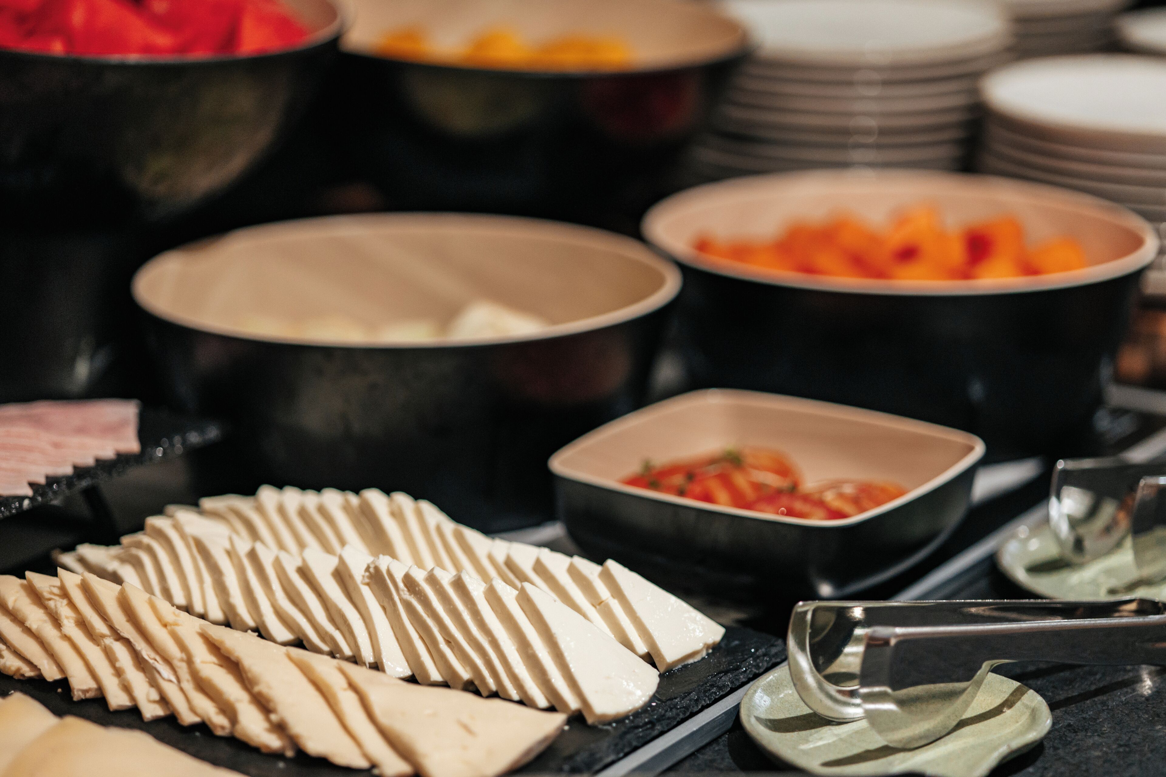 A buffet with various food items including sliced cheese, fruits, and vegetables.