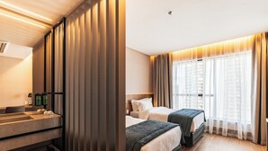Ein Hotelzimmer mit großem Fenster, einem Bett, einem Nachttisch und einem Badebereich mit Waschbecken und Handtuchhalter.