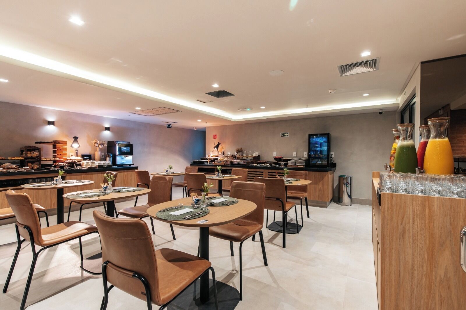 A modern restaurant with round tables and chairs, a bar area with a TV, and a juice bar with colorful drinks.