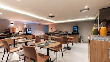 A modern restaurant with round tables and chairs, a bar area with a TV, and a juice bar with colorful drinks.