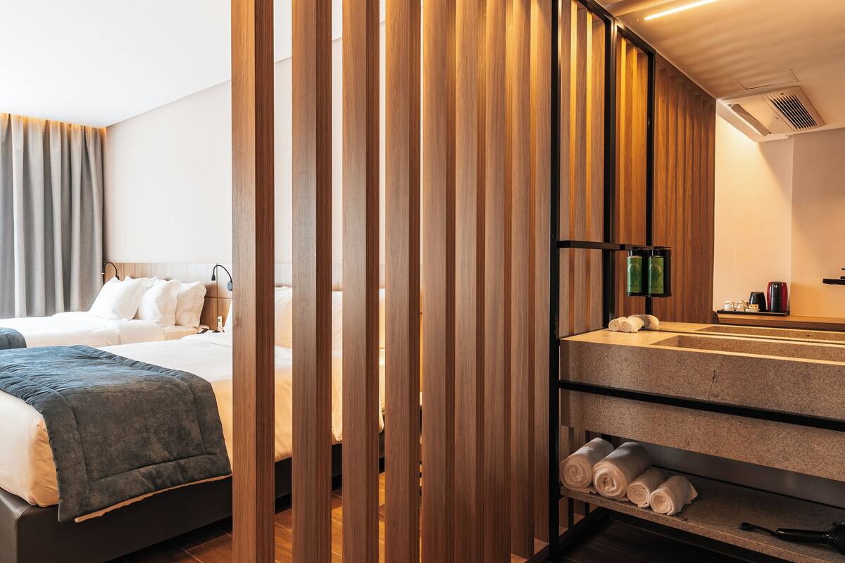Ein modernes Hotelzimmer mit einer Holzwand, einem Bett, einem Badezimmer mit Waschbecken und Handtuchhalter sowie einem Holzboden.