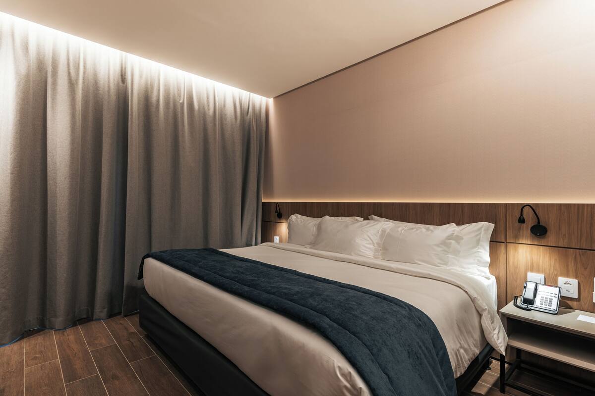 Ein Hotelzimmer mit einem Bett, Vorhängen, einem Nachttisch mit Telefon und einer Wandleuchte.