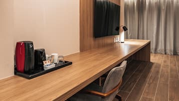 Una habitación de hotel moderna con un escritorio de madera alargado, un televisor de pantalla plana montado en la pared, una cafetera y una silla.