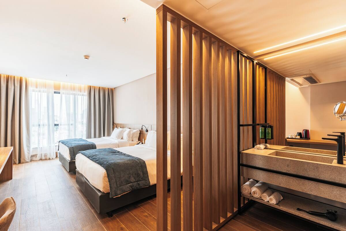 Ein Hotelzimmer mit zwei Betten, einer Holzwand, einem Badezimmer mit Waschbecken und Spiegel sowie einem Schreibtisch.