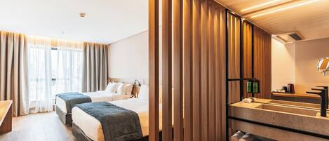 Habitación de hotel con dos camas, un separador de madera, un baño con lavabo y espejo, y un escritorio.