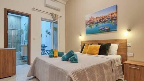 A hotel room with a bed, a painting of a coastal scene, and a view of the outside.