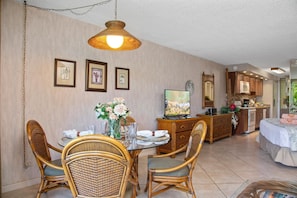 Zona pranzo con sedie in vimini, un tavolo rotondo e un lampadario. Si nota una televisione su un mobile in legno, e sullo sfondo si intravede una cucina.