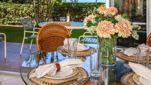 An outdoor dining area with wicker chairs, a glass table, and a vase of flowers. - Maui Kaanapali Villas MKV-C152 by KBM (Kaanapali)
