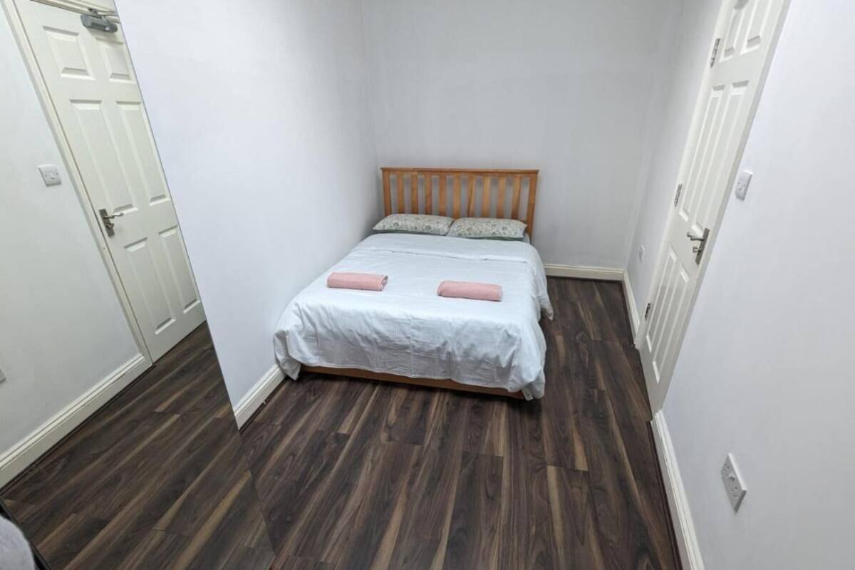 A small, narrow room with a bed, wooden floor, and white walls.