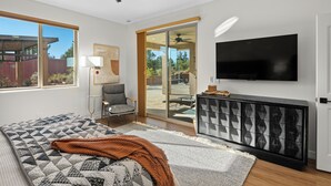 A modern living room with a large bed, a flat-screen TV, a ceiling fan, and a sliding glass door leading to an outdoor patio. - Stylish West Sedona Oasis. Hot Tub, E-BIKES & Kids Play Area (Sedona)