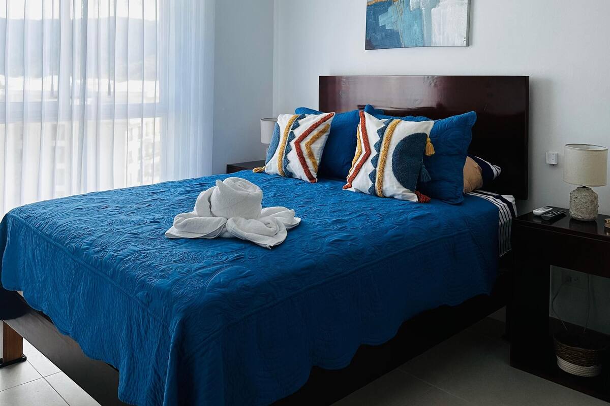 A hotel room with a large bed, a headboard, a nightstand, a lamp, and a painting on the wall.