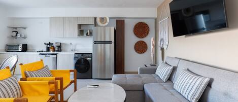 Ein modernes Wohnzimmer mit einem grauen Sofa, gelben Sesseln, einem runden Couchtisch und einer Küchenzeile im Hintergrund.