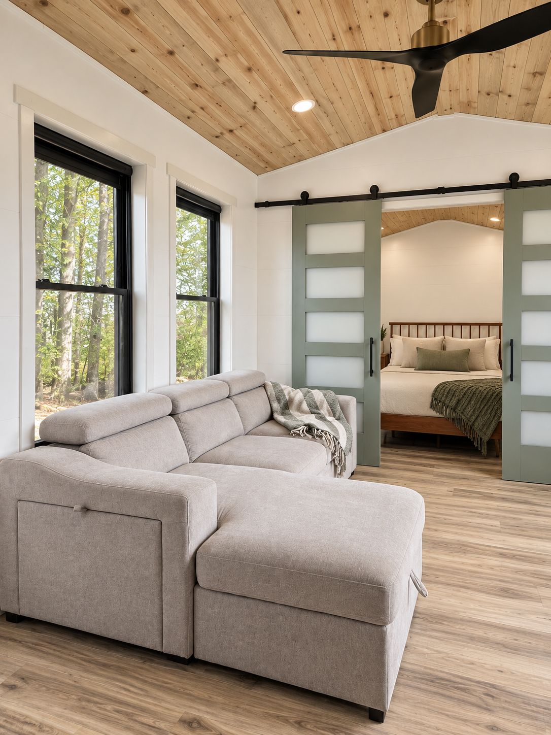 Un intérieur moderne avec un canapé d’angle, un lit avec une tête de lit et un ventilateur de plafond.