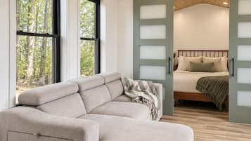 Un intérieur moderne avec un canapé d’angle, un lit avec une tête de lit et un ventilateur de plafond.