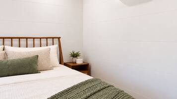 Ein Schlafzimmer mit Holzbalkendecke, einem Bett mit weißer und grüner Decke, einem Nachttisch mit Pflanze und einer Klimaanlage an der Wand.