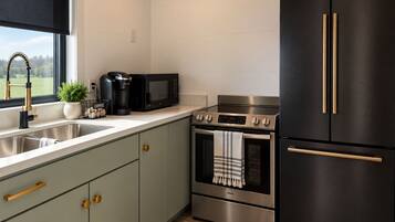 Een moderne keuken met een roestvrijstalen fornuis, oven en een zwarte koelkast met gouden handgrepen.