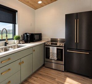 A modern kitchen with a stainless steel stove, oven, and black refrigerator with gold handles.