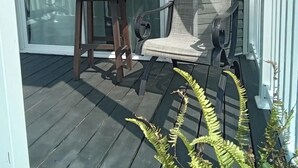 Eine überdachte Veranda mit Tisch und Stühlen, eine Schiebetür und ein weißes Geländer.