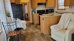 Eine kleine Küche mit Holzschränken, einem schwarzen Kühlschrank, einer Mikrowelle und einer Essecke mit Tisch und Stühlen.
