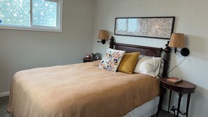 A bedroom with a large bed, two bedside lamps, a nightstand, and a window with frosted glass.